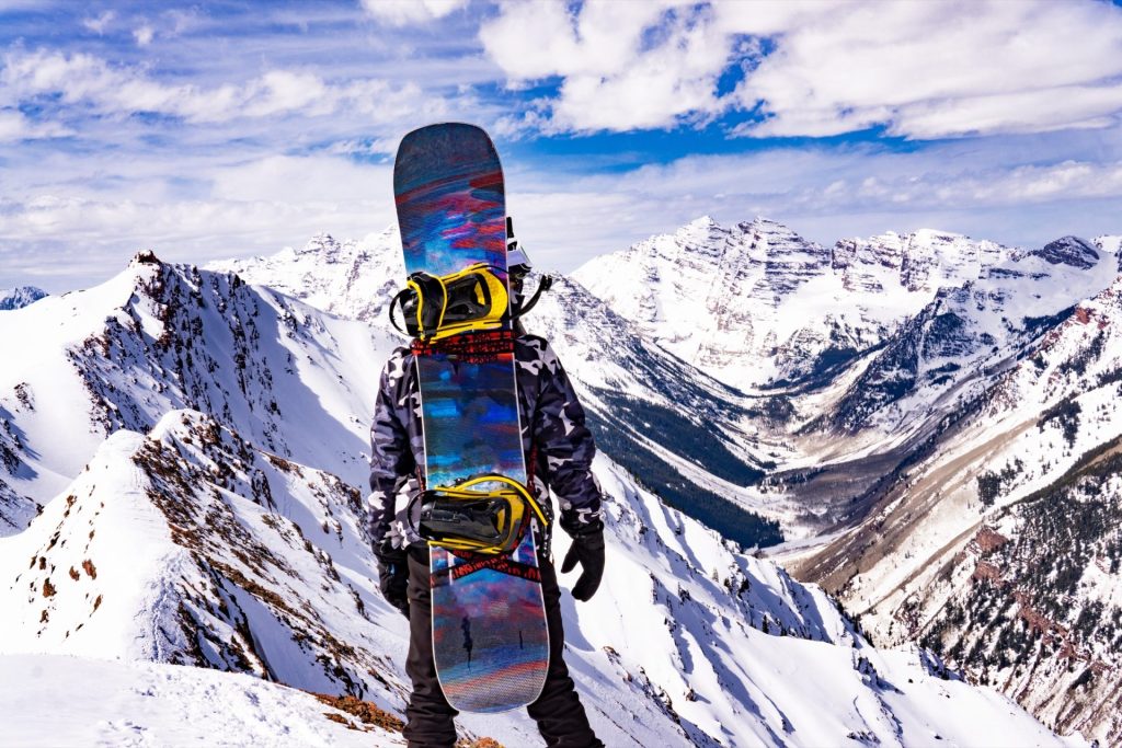 Snowboardeur portant sa planche face aux sommets enneigés