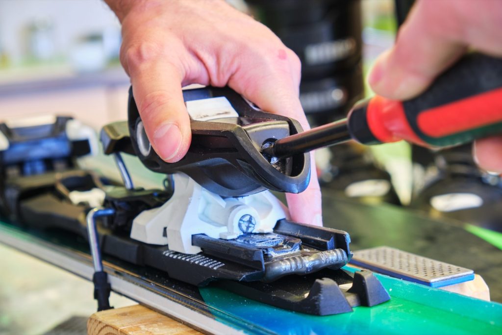 Main réglant une fixation de ski avec un tournevis